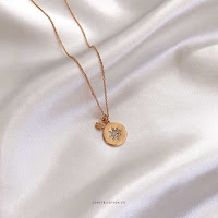 Gold Supernova Star Coin Cendant Necklace by Constellation Co UK, lay on satin white sheets.