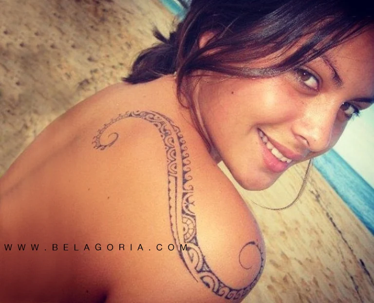 Foto de una modelo riendo mojada en la playa, lleva tatuaje maori en el hombro