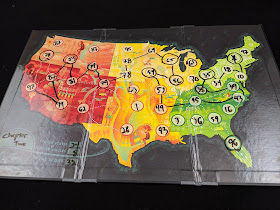 A closer view of one of the game boards, showing a variety of numbers written on the spaces for each state in dry-erase marker, with a route marked between several of these states. In the lower left corner, the band's name 'Chapter Two' has been written, next to the points (24 states + 8 circles = 32 points total).