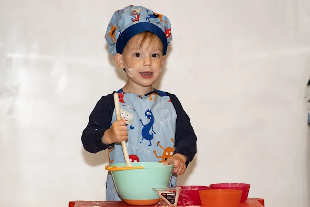 A preschooler with flour on his face mixing a cake together