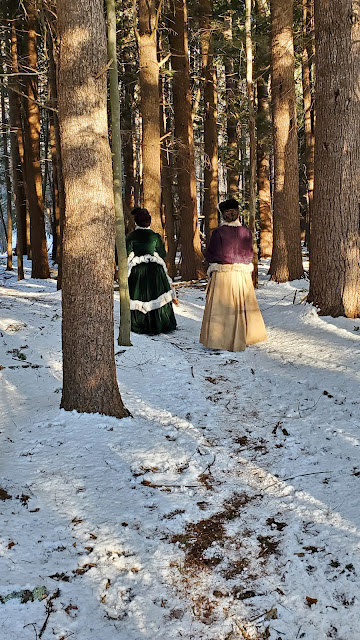 the author and friend in bustle ensembles trekking through a snowy forest