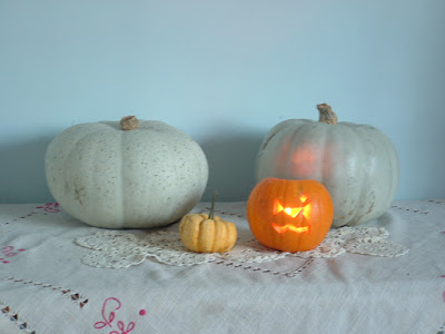 Four pumpkins of various sizes and colors on a table, one a small carved jack o'lantern