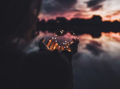 Sunset with a woman holding up fairy lights in the foreground