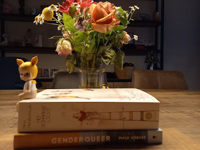 Donny zit op de boeken, die gestapeld zijn. Erachter een bosje bloemen