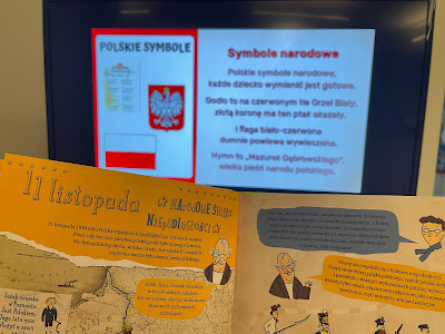 Na pierwszym planie znajduje się trzymana w dłoni książka otwarta na stronie z informacjami na temat Narodowego Święta Niepodległości. W tle widać telewizor ze slajdem pn. Symbole narodowe.