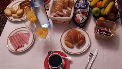 mesa com xícara de café, pães, frutas, suco de laranja garrafa de água, fiambre e compotas