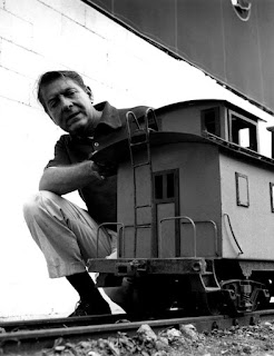 Fotografía de David Rose en blanco y negro junto a la maqueta de un vagón de tren antiguo en 1959