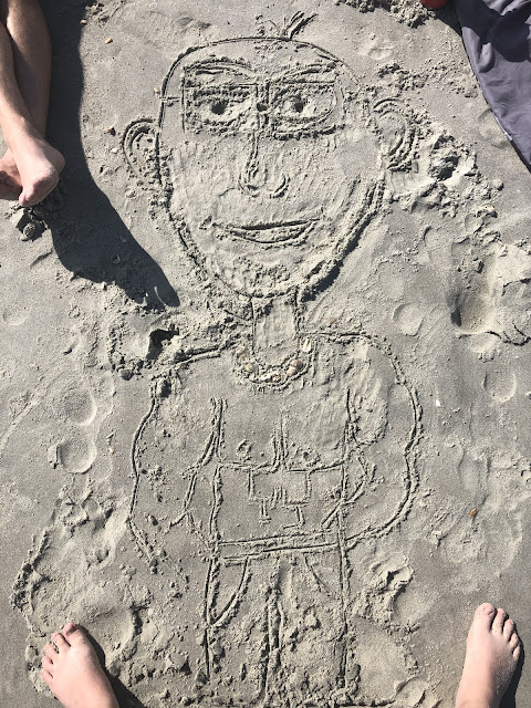 A drawing Elizabeth made of a bald muscular man with a six-pack in the sand.