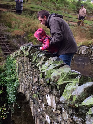 Daddy standing on a stone bridge holding up toddler to look over it