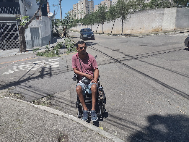 Rapaz em cadeira de rodas ao lado de calçada sem rampa de acesso