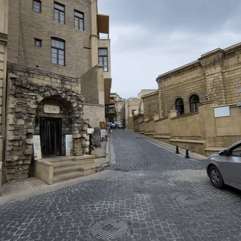 A narrow cobblestone street in Baku’s Old City lined with historic sandstone buildings and a cozy local café entrance.