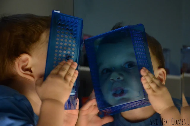 A toddler holding up a plastic container to his face