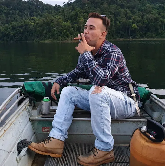 2/2 chilling in a boat fishing with nice combat boots blue jeans that are wearing at the knees flannel smoking a cigar