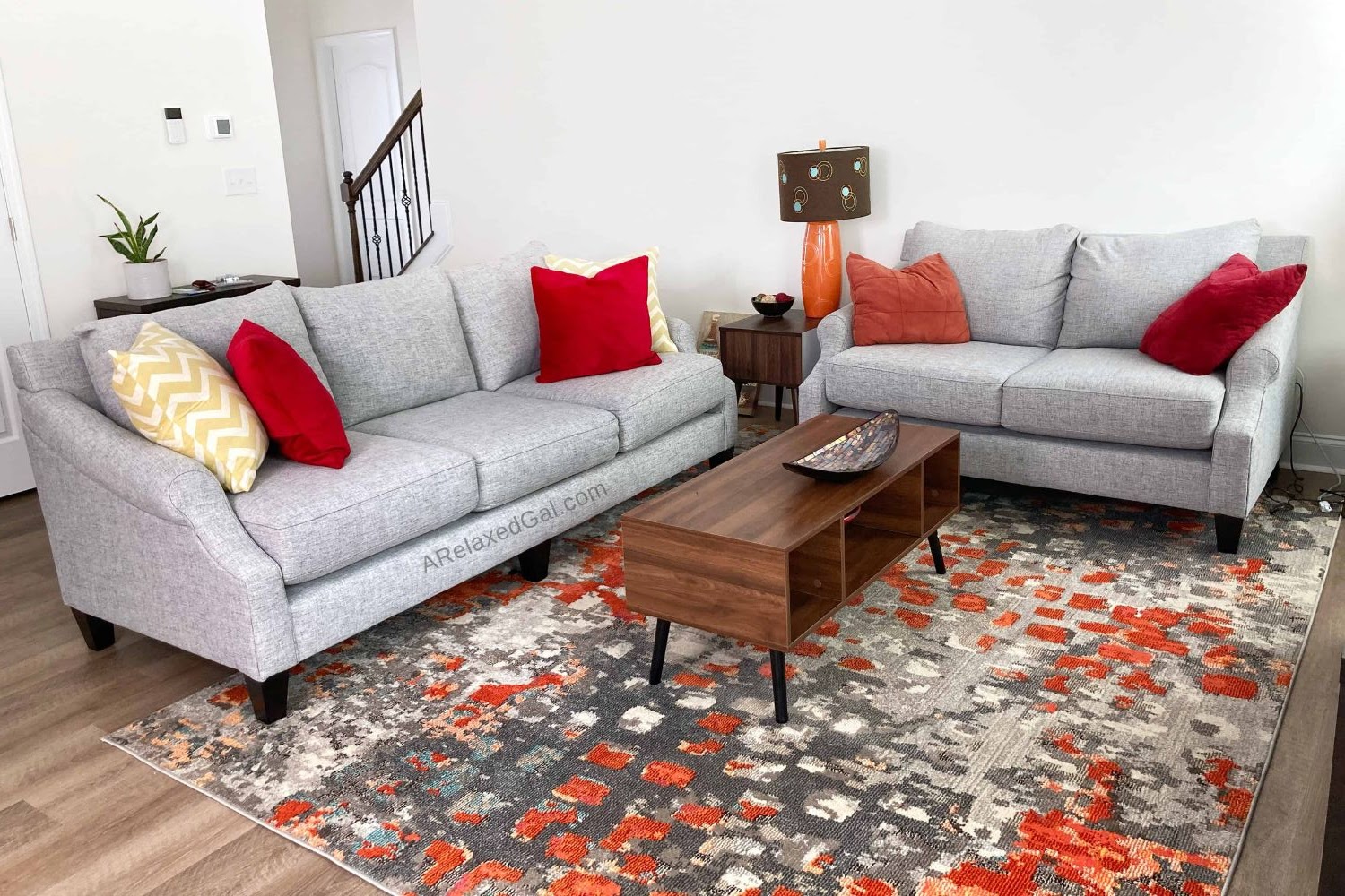light grey couch and loveseat with pretty orange rug and lamp.