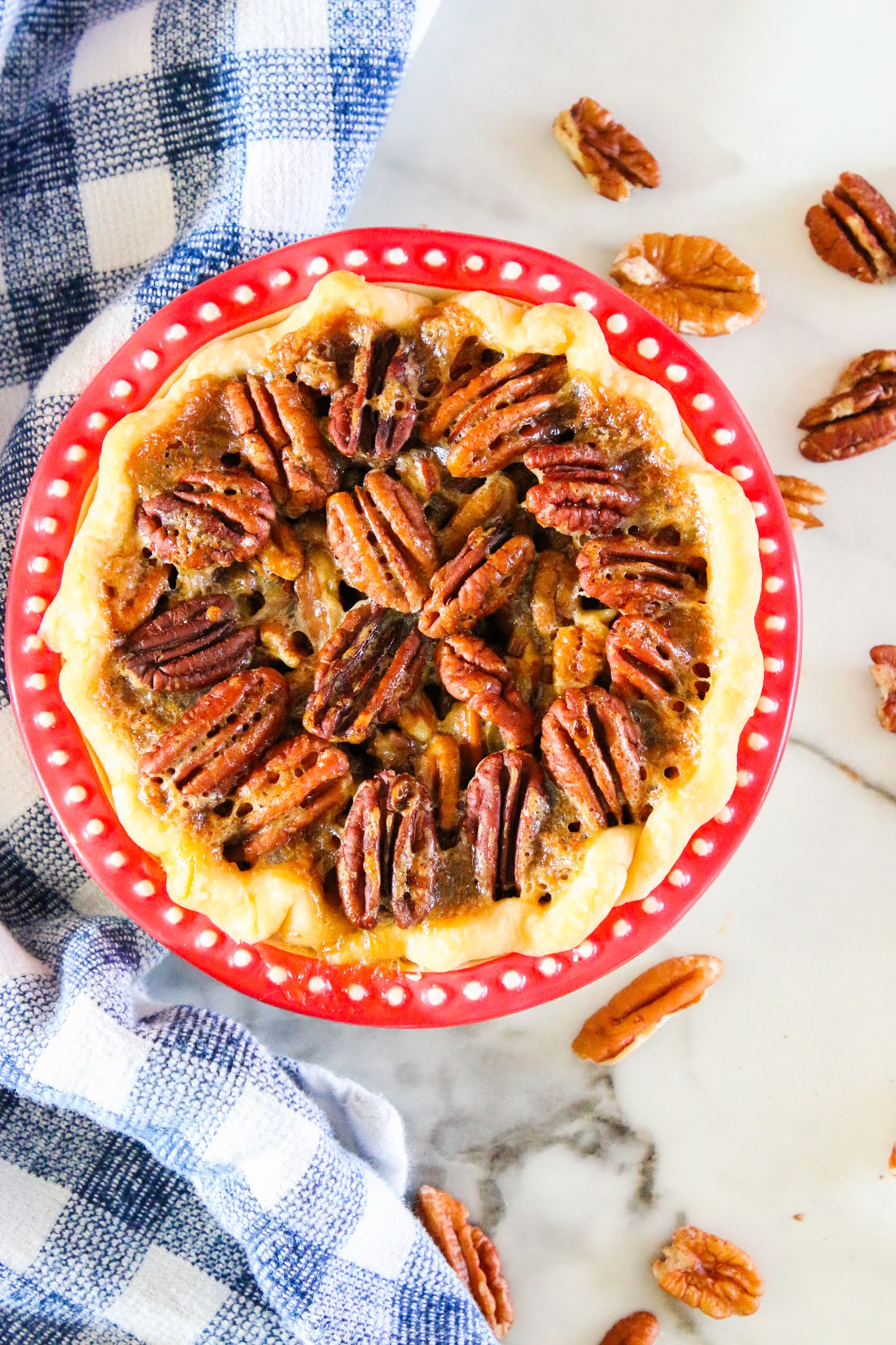 Pecan pie in a red pie dish with a blue dish towel in the background.