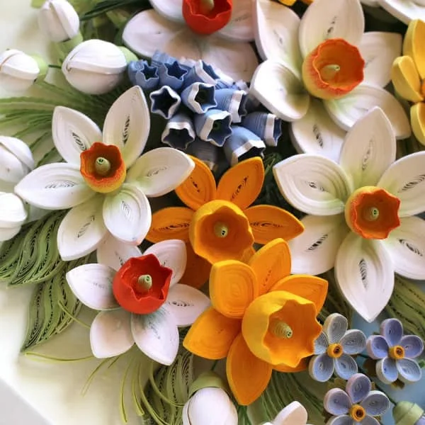 close up view of quilled white and yellow daffodils and small blue flowers