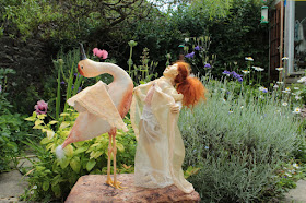 Birth Dance sculpture by Corina Duyn. A bird and a young girl, of same size, pictured in a summer garden 