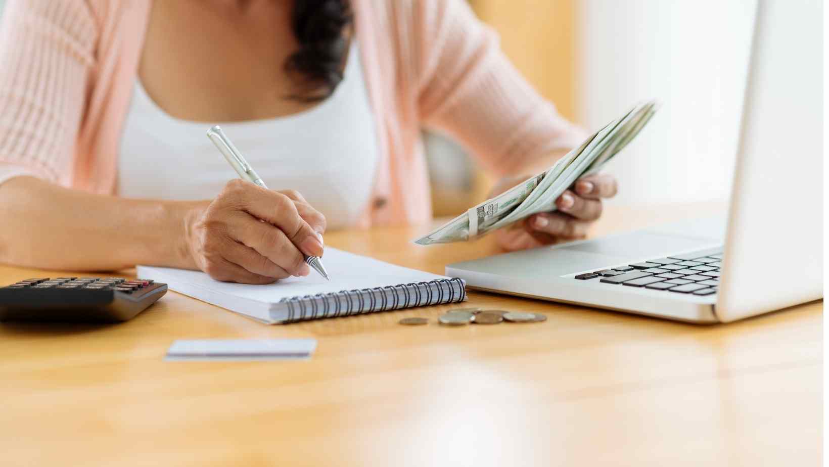 A free stock image from canva pro showing a woman at a table working on her monthly budget for her household