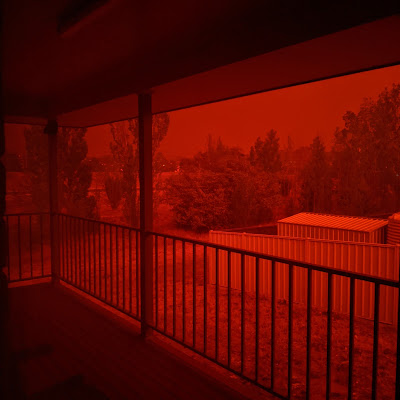 A view out a window of a world that is red due to smoke from fires in the region covering the sun.