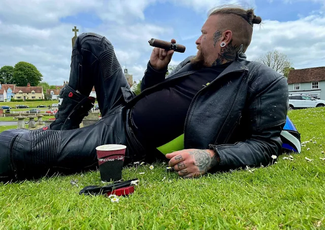 Blonde biker laying in the grass smoking a cigar with full leather gear on