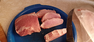 Half of a pork roast left whole with other half cut into pork chops, all sitting on a blue tray.