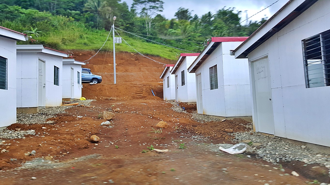 rows of newly built temporary shelters in uneven terrain