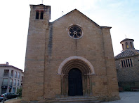 La façana de ponent amb la portalada romànica, la rosassa i la torre que permet pujar a la teulada. A la dreta de la imatge es veu l'església nova