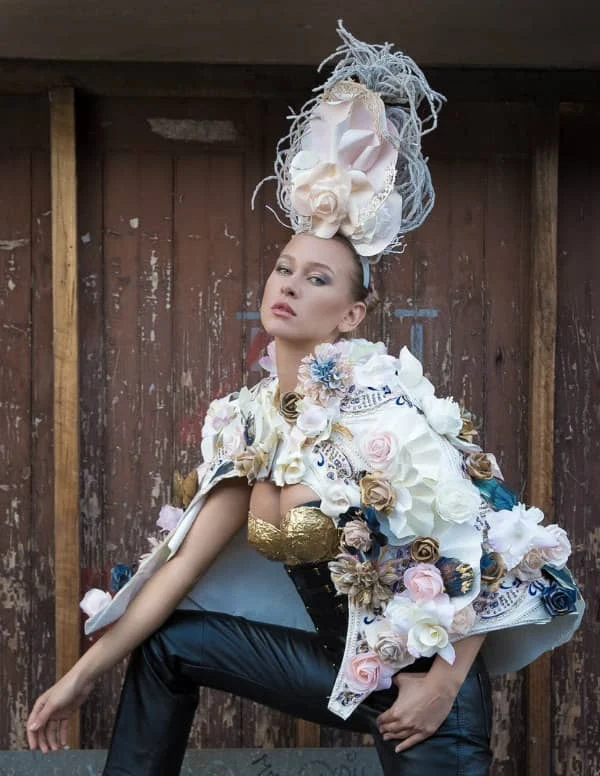 young female model wearing ornate paper flower headpiece and floral cape over gold paper brassiere