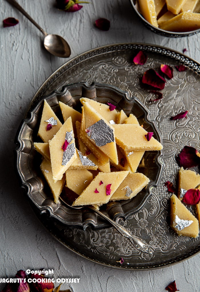 Over head shot of no added sugar badam katli in instant pot served in a metal bowl and garnished with red dried rose petals