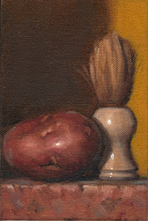 Still life oil painting of a Désirée potato beside a shaving brush.