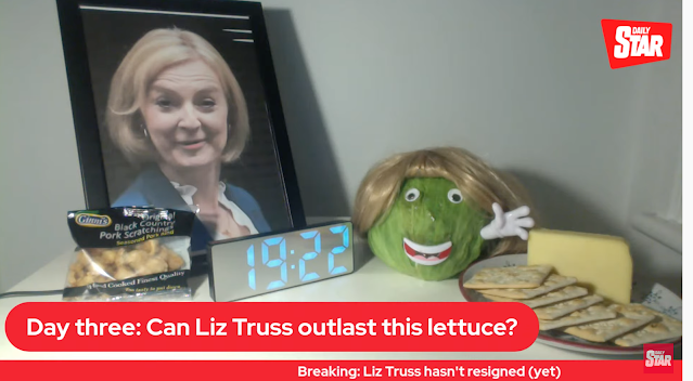 Daily Star screenshot: Day Three: can liz truss outlast this lettuce?  Iceburg lettuce with face and wig, surrounded by pic of Liz Truss, snack foods, and clock reading 19:22