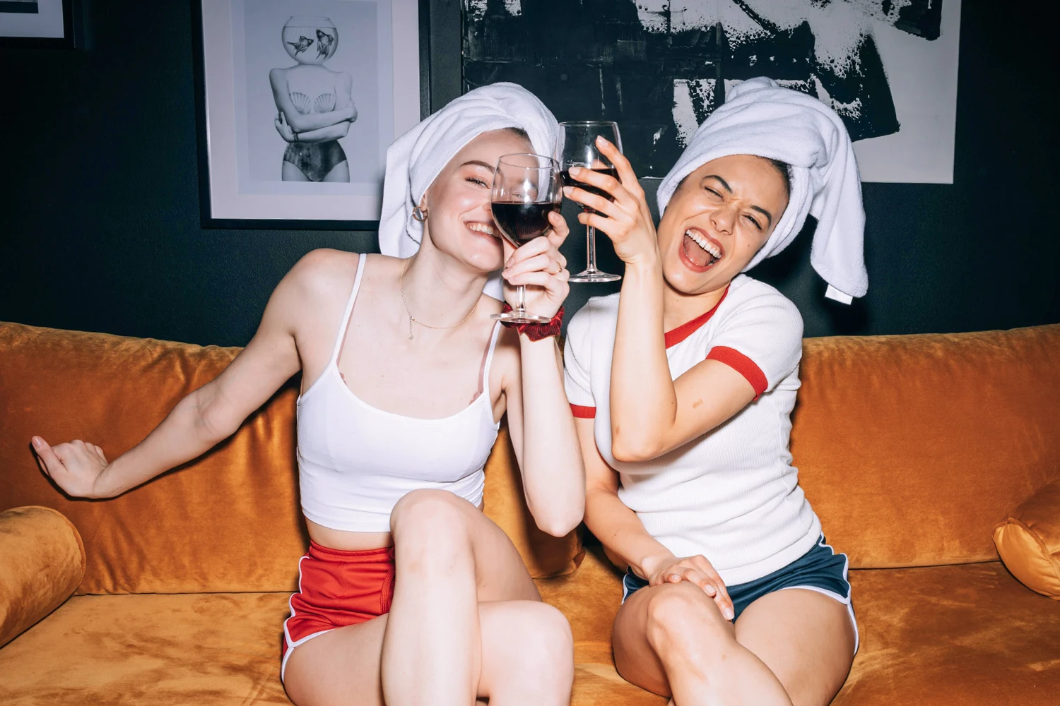 two smiling women drink wine and pose for the camera