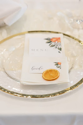 white menu fold napkin with white and orange napkin and orange slice placed on gold rimmed charger
