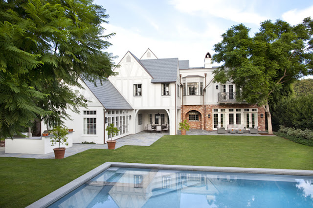 exterior of a white and brick Tudor home in Beverly Hills with a backyard, pool, and grass