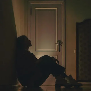 A sad girl sitting in the darkness near the door.