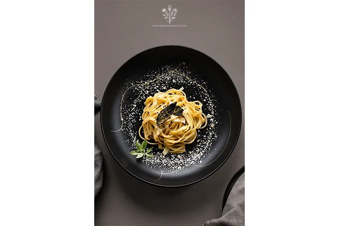 Elegant plating of Black Truffle Pasta with Parmesan, twirled on a black plate, garnished with fresh truffle shavings, parmesan, and a delicate herb sprig.