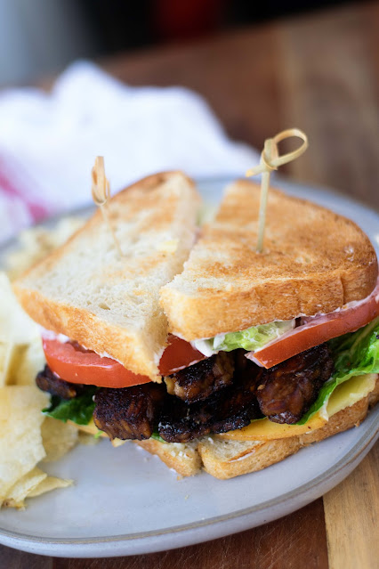 The tempeh blt on a plate with chips.