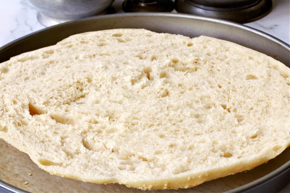 Muffuletta Bread cut side up in a pizza pan.