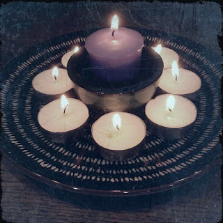 Purple candle burning in the centre of a circle of burning tealights