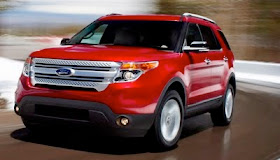 Front 3/4 view of a red 2011 Ford Explorer driving on a wet winding road