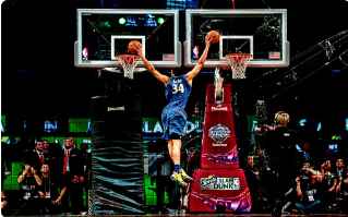 Basketball player wearing blue baksetball clothing shooting two basketballs into basketball nets at the same time