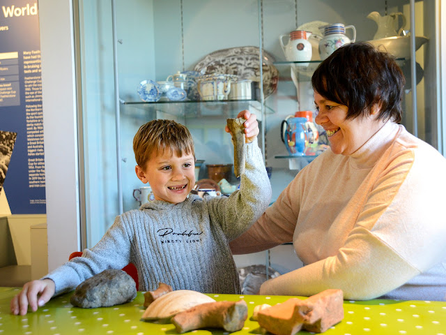 A young visitor and their grown-up handling archaeological objects at Castleford Museum