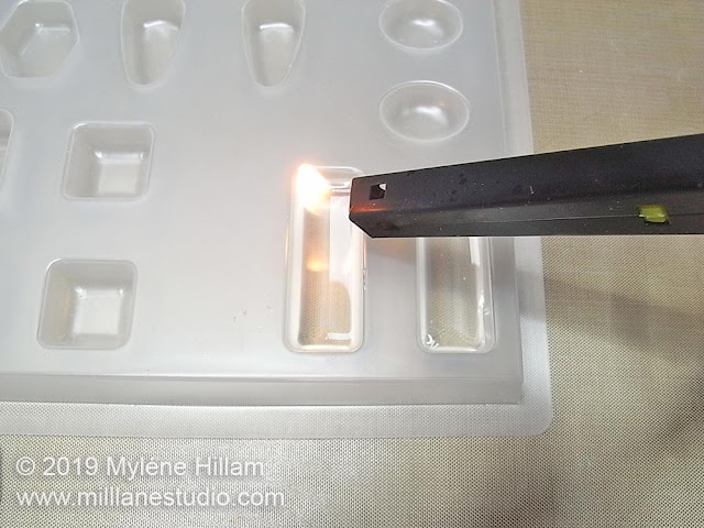 Using a flame to pop the bubbles in the resin.