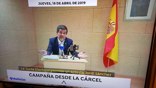 Jordi Sánchez, durante su conferencia de prensa, con la bandera de España y el retrato del Rey como telón de fondo del escenario carcelario (Foto de Internet)