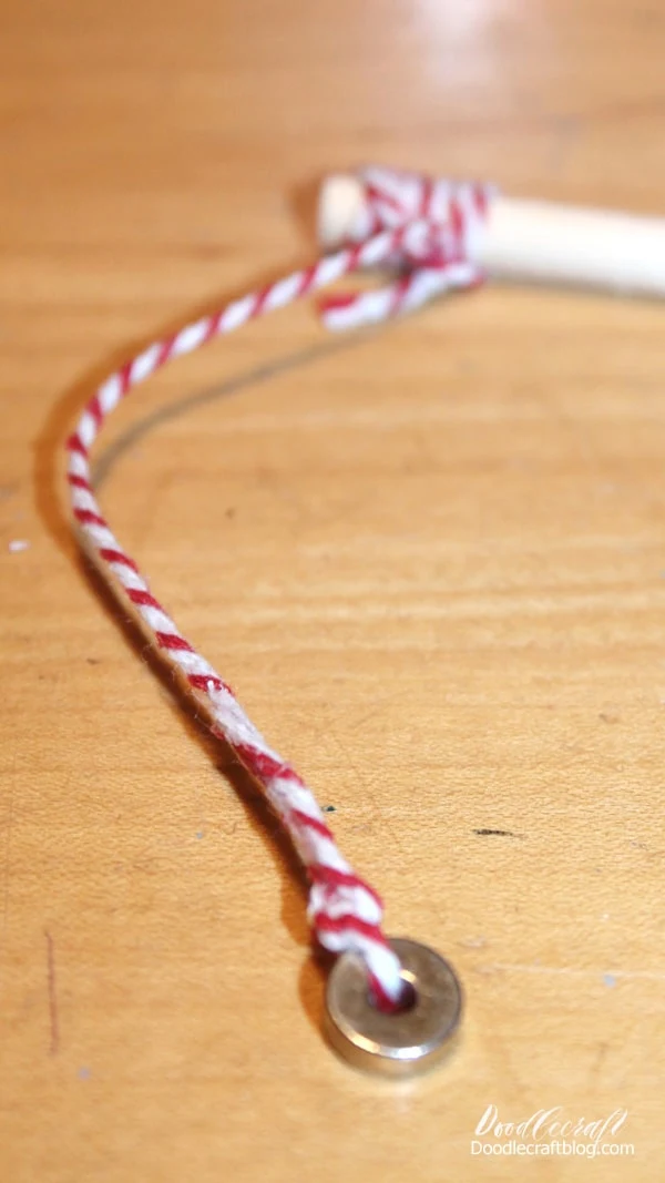 Tie and hot glue twine onto the end of the dowel. Hot gluing it firmly in place is ideal for small children.   Then tie the donut magnet on the end of the twine. The twine can be as long as you want, anywhere from 6-12 inches for a small Altoids tin.