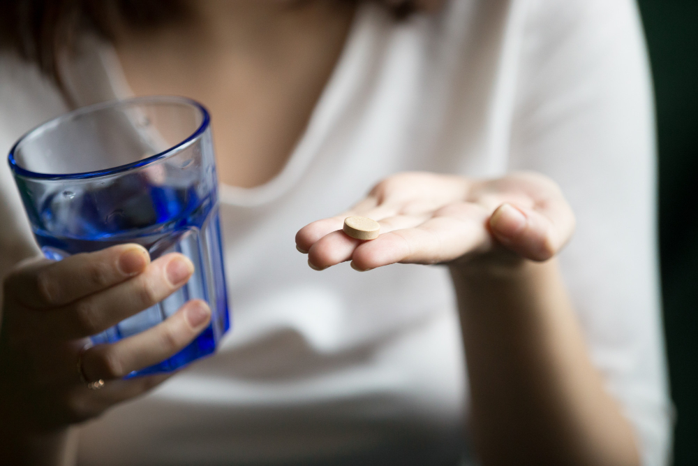 woman holding a pill in open hand a water glass in the other