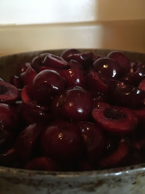 A ceramic bowl full of black-red halved and pitted cherries, shiny and juicy.