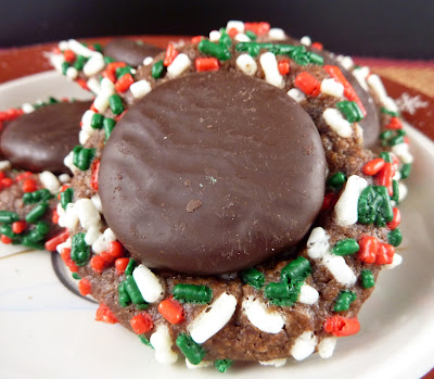 A chocolate thumbprint cookie, covered with Christmas sprinkles and a York Peppermint Patty for the thumbprint. Photographed on a white plate with a red trim.