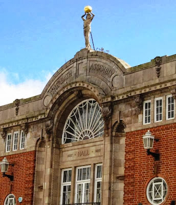 Art deco frontage topped by statue of a woman holding aloft a large golden ball