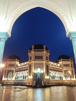  Masjid Raya AL- Mashun Medan Tempat wisata Religi yang kini berusia 113  Tahun  Medan seperti tak ada habisnya untuk ditelusuri, kamu yang suka wisata sejarah atau heritage seperti Saya pasti tak akan melewatkan tempat yang satu ini, yah Masjid Raya Al- Mashun Medan meninggalkan banyak sejarah di dalamnya. Masjid yang berlokasi tak jauh dari pusat kota Medan ini terletak di Jalan Sisingamangaraja No.61Medan Maimun. Pembangunan Masjid Al- Mashun sendiri dimulai pada tanggal 21 Agustus 1906 (1 Rajab 1324 H) oleh Sultan Ma’mun Al- Rasyid Perkasa Alam yakni pemimpin Kesultanan Deli pada masa itu. Dan secara keseluruhan pembangunan selesai pada tanggal 10 september 1909 yang artinya waktu pembangunan yang dibutuhkan adalah 3 tahun lebih. Dilansir dari Simas.kemenag.go.id Masjid yang Luas bangunannya sampai 5.000 m2 menelan biaya pembangunan mencapai satu juta Gulden. Kemudian Masjid ini juga ini memiliki daya tampung hingga 1.500 jamaah. Masjid yang dibangun di atas lahan seluas 18.000 kini sudah memasuki usia satu abad lebih, tepatnya berumur113 Tahun.  Menurut sejarahnya, Sultan Ma’mun Al-Rasyid memang sengaja membangun Masjid ini dengan megah, karena menurut prinsip nya hal itu lebih utama ketimbang kemegahan Istananya sendiri, yakni Istana Maimun yang berjarak 200m dari Masjid. Kemudian, pembangunan Masjid ini ditanggung sendiri oleh Sultan Ma’mun Al- Rasyid, namun konon katanya Tjong A Fie, tokoh saudagar kaya dari etnis Tionghoa ini pun turut berkontribusi dalam pendanaan pembangunan Masjid Raya ini. Pada mulanya arsitek yang merancang bangunan Masjid Raya ini merupakan Van Erp arsitek asal Belanda yang sebelumnya juga merancang Istana Maimun, namun kemudian prosesnya dikerjakan oleh JA Tingdeman. Alasanya karena ketika itu Van Erp dipanggil ke pulau Jawa oleh pemerintah Hindia Belanda untuk bergabung dalam proses restorasi candi Borobudur di Jawa Tengah. Kemudian JA Tingdeman merancang masjid ini dengan denah simetris segi delapan dalam corak bangunan campuran Maroko, Eropa dan Melayu serta Timur Tengah.  Pada bangunan masjid dibagi atas beberapa ruang utama, tempat wudhu, gerbang masuk dan menara. Ruang utama, tempat sholat berbentuk segi delapan tidak sama sisi. Pada sisi berhadapan lebih kecil, terdapat beranda yakni serambi kecil yang menempek menjorok keluar. Di bagian dalam masjid terdapat pilar utama berdiameter 0.60 m yang menjulang tinggi. Masjid Raya Al- Mashun didominasi warna putih, di samping hijau pada sekitar bagian pintu-pintu dan warna hitam pada kubahnya. Pilar-pilar yang terdapat pada setiap sisi bangunan untama mengambil corak khas Cordoba dan spanyol, terutama dengan lekung bagian atas yang berbentuk setengah lingkaran. Untuk membangun Masjid Raya Al- Mashun banyak dekorasi yang diimpor dari mancanegara seperti marmer dari Italia, kaca patri asal Cina, dan lampu gantung dari Prancis. Seriap ornamen dihiasi dengan ukiran-ukiran indah bermatif floral atau geometris. Keindahan Masjid Raya Al-Mashun dan Istana Maimun menandakan tingginya peradaban Kesultanan Deli, sebagai suatu kedaulatan etnis Melayu yang sempat berjaya pada zaman lampau. 